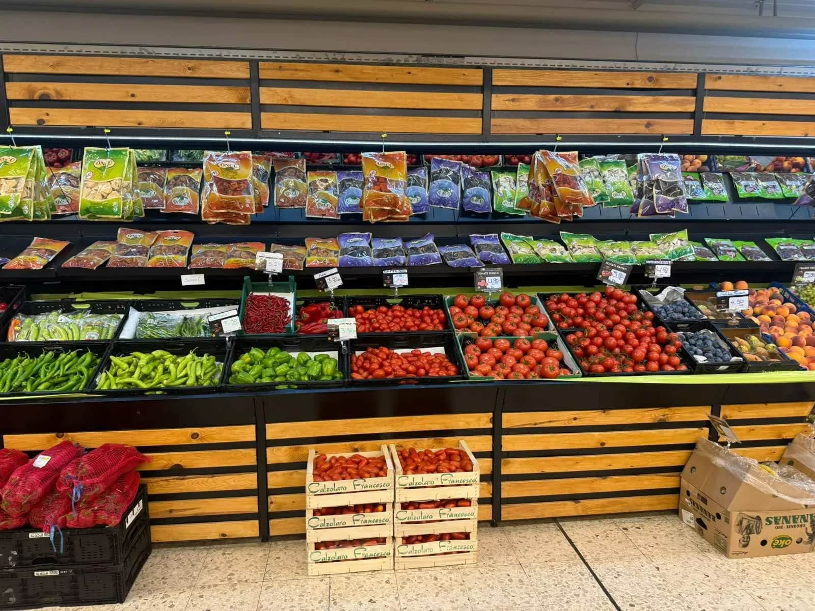 Gemüseregal mit Beeren, Tomaten und Kartoffeln in Holzkisten